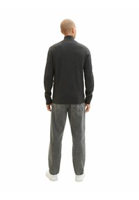 Szary sweter dzianinowy z wysokim kołnierzem, zestawiony z luźnymi szarymi dżinsami i białymi butami, widziany z tyłu na białym tle.