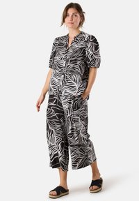 Zwart-wit gemusterde jumpsuit met korte pofmouwen, knoopsluiting aan de voorkant en wijde pijpen. Zacht, lichtgewicht stof.