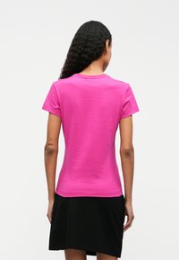 Tricou scurt cu mâneci scurte, de culoare roz aprins, fabricat dintr-un material de bumbac neted. Guler rotund, spate simplu și croială care ajunge până la șold.