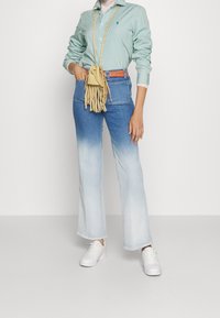 Zelené a bílé pruhované tričko s dlouhým rukávem, modré džínové široké kalhoty, béžová kabelka přes rameno s třásněmi a bílé tenisky.