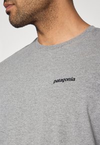 Γκρι βαμβακερό T-shirt με στρογγυλή λαιμόκοψη και κοντά μανίκια. Εμφανές μαύρο λογότυπο "patagonia" κεντημένο σ το αριστερό στήθος. Μαλακή υφή.