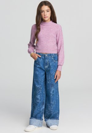 Maglione cropped a maniche lunghe di colore rosa glitterato abbinato a jeans a gamba larga blu sbiaditi con motivo floreale e orli risvoltati. Le sneakers completano il look.