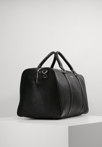 Black leather duffle bag with rounded edges, dual top handles, front zipper, and subtle stitching details. Smooth texture and sleek design.