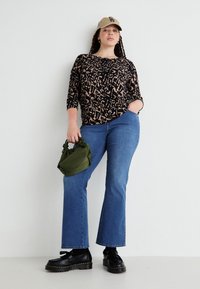 Svart och brun leopardmönstrad topp, blå utsvängda jeans, svarta platåskor och en olivgrön handväska, bärs med en beige keps.