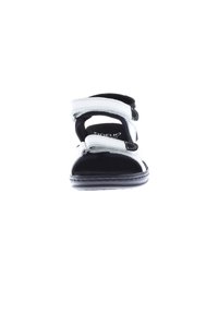 White sandal with adjustable Velcro straps, black accents, and textured footbed. Smooth sole with rounded toe design. Brand logo visible.
