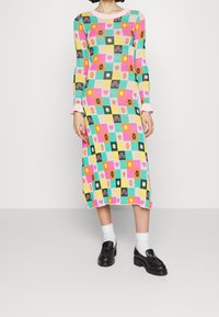 Robe tricotée mi-longue avec un motif en damier multicolore. Dotée de manches longues, d'un col rond rose et de poignets côtelés.