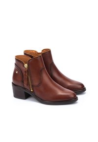 Botas de cuero marrón hasta el tobillo con punta afilada, cremallera lateral y borlas decorativas. Tacón cuadrado y textura suave con un diseño minimalista.