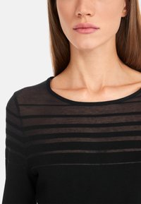 Schwarzes Oberteil mit runder Ausschnitt und horizontalen transparenten Streifen im Torso. Weiche Textur mit taillierter Passform.