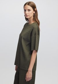 Olive green oversize t-shirt wykonana z żebrowanej tkaniny, z krótkimi rękawami i okrągłym dekoltem. Prosty krój, teksturowana powierzchnia, luźny fason.