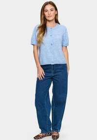 Jasnoniebieski kardigan z krótkim rękawem, okrągłym dekoltem, z przodu zapinany na guziki i z ribbowym wykończeniem, zestawiony z ciemnoniebieskimi dżinsami oraz balerinami w panterkę.