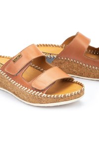 Chanclas de cuero marrón con dos correas anchas, plantilla de corcho y acentos de costura blanca. Suela plana y diseño de punta abierta para una mayor transpirabilidad.
