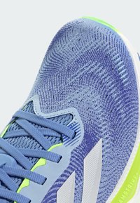 Blue athletic shoe featuring a textured knit upper, grey accents, reflective details, and a white sole with vibrant green highlighting.
