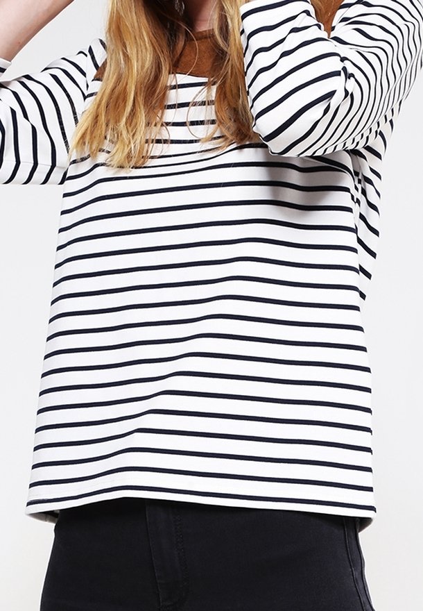 Vit långärmad topp med marinblå horisontella ränder, rund halsringning och avslappnad passform, kombinerad med svarta byxor. Mjuk tygkänsla.