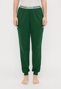 Grønne bomullssweatpants med en hvit- og grønnstripet elastisk midjebånd, innsnevring ved bena og ribbede mansjetter. Ingen lommer.