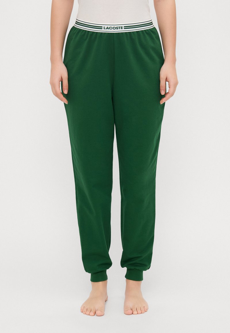 Grønne bomullssweatpants med en hvit- og grønnstripet elastisk midjebånd, innsnevring ved bena og ribbede mansjetter. Ingen lommer.