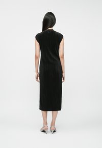 Fekete, midi hosszúságú ruha, batikolt ujjal, redőzött textúrával és testhez simuló szabással. Szürke magassarkú szandálokkal viselve.