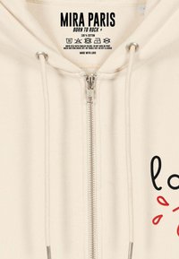 Felpa con zip color beige realizzata in 100% cotone, con zip argentata, cordini e testo grafico nero/rosso sul davanti.