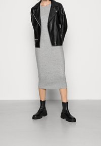 Veste de motard en cuir noir portée sur une robe midi grise côtelée, associée à des bottines noires épaisses. Textures lisses et coupe ajustée.