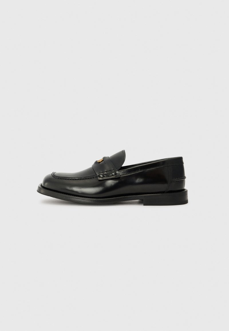 Must must tömbiga, ümmarguse varbaga must nahast loafers, dekoratiivse õmblusega ja väikese esise palakaga. Lame kummist tald, millel on minimaalne kand.