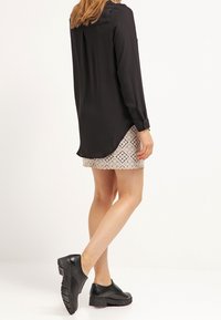 Camisetta nera a maniche lunghe con una leggera lucentezza, abbinata a una gonna chiara a fantasia. Scarpe nere con tacco largo completano l'outfit.