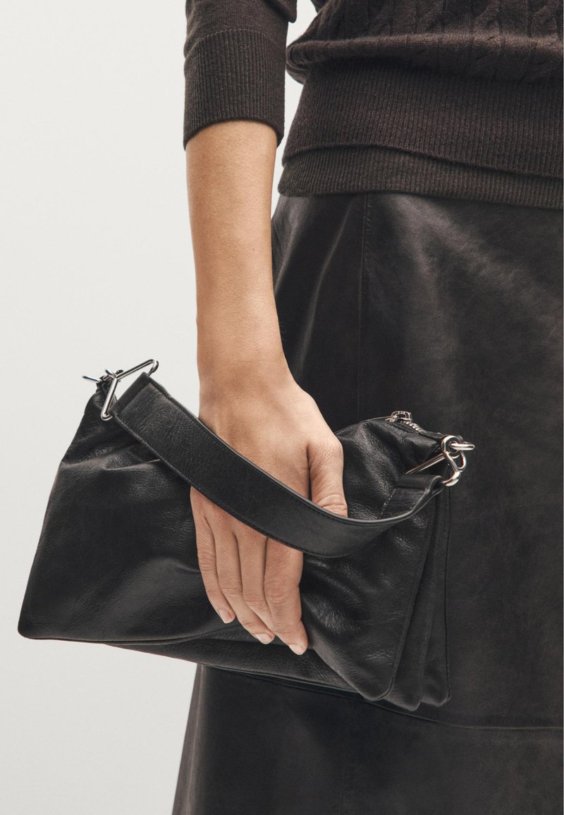 Borsa a mano in pelle nera con un design strutturato, caratterizzata da una forma piatta, una superficie texturizzata e una tracolla removibile con accessori metallici.