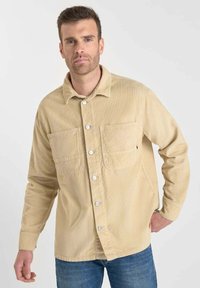 Beige corduroy overhemd met een kraag, knoopsluiting en twee opgestikte zakken. Heeft een gestructureerd oppervlak en lange mouwen.