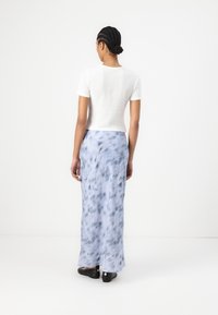Haut blanc à manches courtes à côtes associé à une longue jupe bleu clair avec un motif tie-dye et une légère évasement. Chaussures noires.