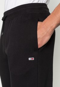 Svarta sweatshirtbyxor med resårmidja, sidofickor och en liten broderad logotyp med röd, vit och blå accent vid fickan.