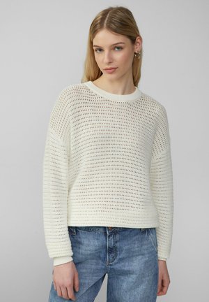 Wit gebreid sweater met een losse pasvorm, met een gaasontwerp, brede mouwen en ribgebreide manchetten. Gedirigeerd met lichtblauwe denim jeans.