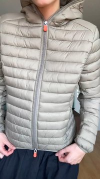 Giacca a vento leggera beige con imbottitura, con cuciture orizzontali, zip frontale e cappuccio. Presenta zip arancioni sulle tasche e una texture distintiva.
