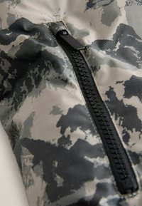 Tissu à motifs gris et noir mettant en avant une fermeture éclair noire proéminente avec des dents texturées, cousue dans un design élégant.