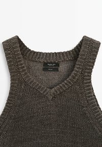 Gilet sans manches en tricot gris foncé avec col en V, bords côtelés et une étiquette de marque visible à l'intérieur du col.