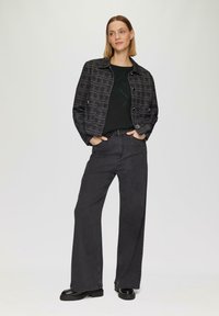 Zwart geruite jas met een kraag en zilveren knopen, gecombineerd met donkere jeans met versieringen en stevige zwarte laarzen.