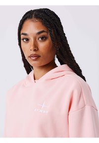 Lichtroze hoodie met een capuchon, een zak aan de voorkant en een wit "PXP"-logo. De stof oogt zacht, met een ontspannen pasvorm en een subtiele textuur.