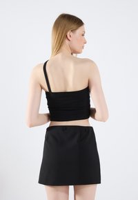 Černý žebrovaný crop top s jedním ramenním popruhem, doplněný o černou mini sukni s dvěma předními kapsami a hladkým povrchem.