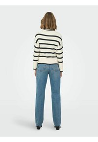 Prugasti džemper s okruglim izrezom u krem i crnoj boji, uparen s trapericama visokog struka u plavoj boji. Kroj je opušten, s rebrastom teksturom.