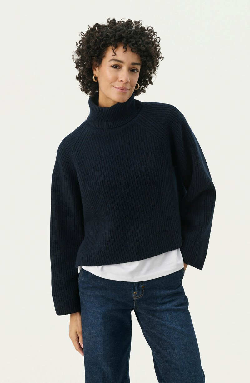 Navy blue ribbed knit turtleneck sweater with a relaxed fit, dropped shoulders, and long sleeves, layered over a white shirt.