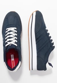 Námořnické modré sportovní boty s bílými tkaničkami, texturovaným materiálem a gumovými podrážkami s hnědým akcentem. Tři vyvýšené pruhy na boku.