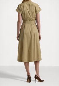Khaki knee-length dress with short rolled sleeves, a fitted waist, and a flared skirt. Brown high heels complete the look.