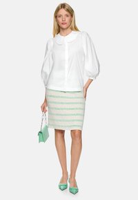 White blouse with a Peter Pan collar and puffed sleeves, paired with a knee-length mint green skirt featuring striped patterns. Holding a mint handbag.