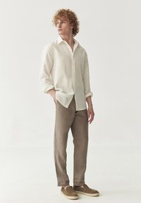 Helle beige Leinenbluse mit hochgekrempelten Ärmeln, kombiniert mit taupefarbigen Hosen und braunen Slippern. Schlichte, lockere Passform mit minimalen Details.