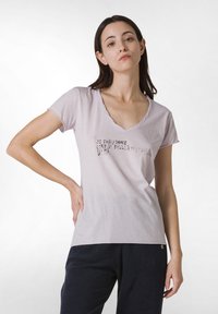 Camiseta de algodón de color rosa claro con escote en V, mangas cortas y texto impreso en el frontal. Textura suave y corte relajado.