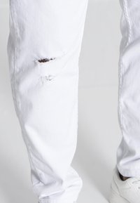 Jeans de mezclilla blanca con un destacado desgastado en la rodilla, diseño recto y tejido texturizado. Acompañados de zapatillas blancas.