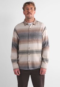 Camicia a maniche lunghe a quadri in beige, marrone e grigio, con chiusura a bottoni e tasca sul petto. Realizzata in un materiale morbido e testurizzato.
