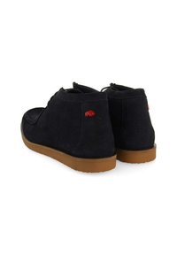 Botas de ante azul marino hasta el tobillo con una suela de goma marrón, que presentan un logo de oso rojo en la parte trasera. Diseño clásico con cordones y una textura suave.