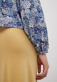 Blusa floreale blu con maniche a sbuffo, abbinata a una gonna liscia beige. Tessuto strutturato, motivi intricati e dettagli con polsini elasticizzati.