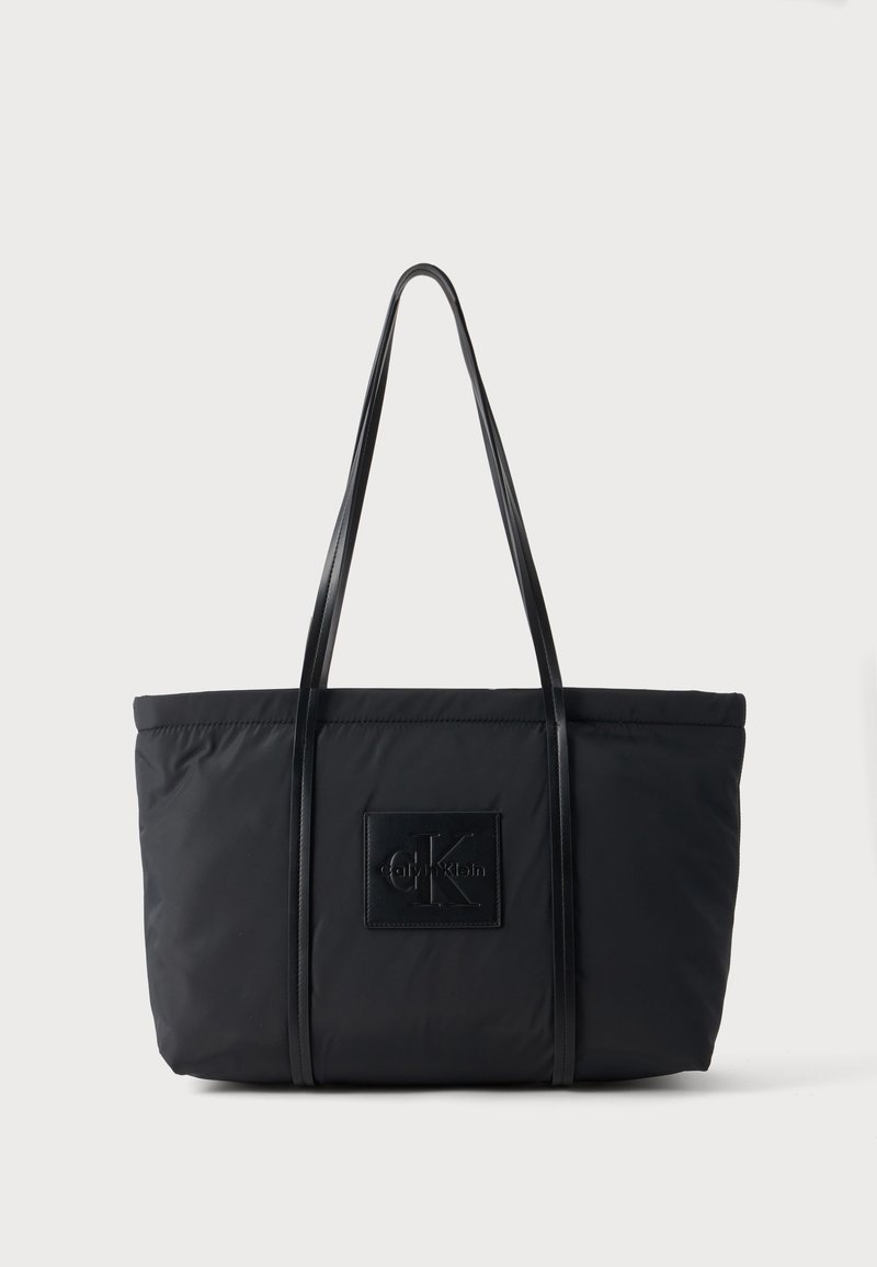 Μαύρη τσάντα Calvin Klein tote με μακριά χερούλια και λογότυπο μπροστά, τοποθετημένη σε απλό ανοιχτό φόντο.