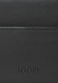 Borsa nera in nylon, caratterizzata da una texture liscia con un accento simile alla pelle, logo "JOOP!" in rilievo e dettagli di cucitura discreti.