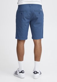Blå, mønstrede shorts med mid-rise talje, to baglommer og lige ben, kombineret med hvide sokker og sko med sorte striber.