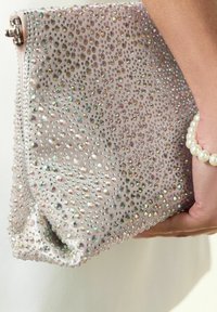 Clutch bag in pale pink fabric adorned with iridescent rhinestones and silver hardware. Zipper closure, structured design, and textured surface.